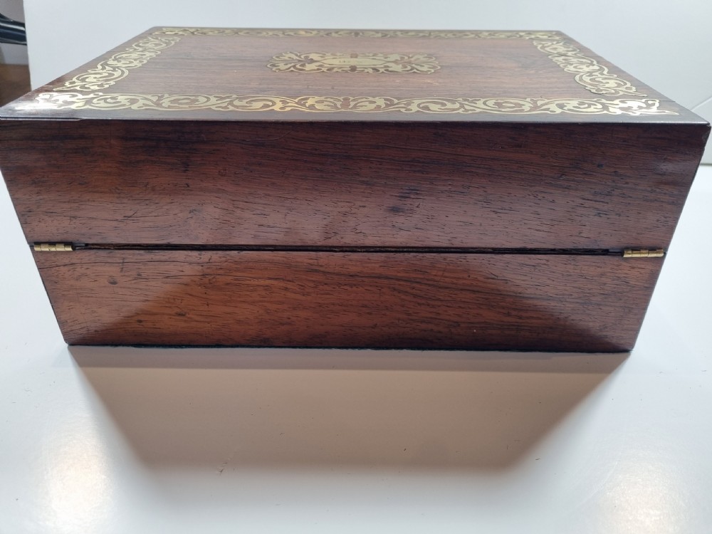 A rectangular dark rosewood writing box featuring intricate brass floral scrollwork inlay around the borders and escutcheon, complete with a key and tassel. View V