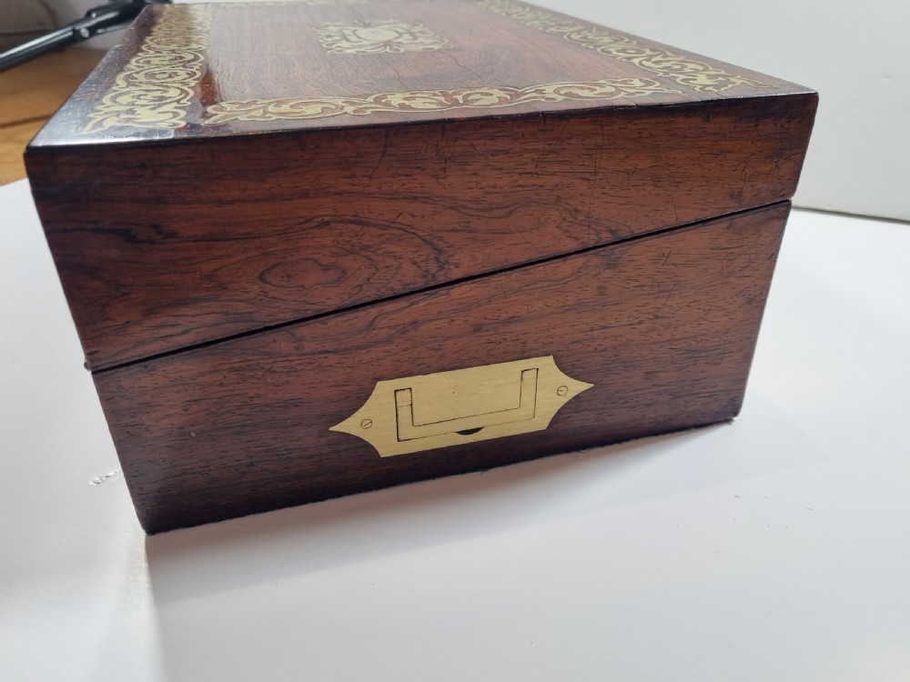 A rectangular dark rosewood writing box featuring intricate brass floral scrollwork inlay around the borders and escutcheon, complete with a key and tassel. View VI