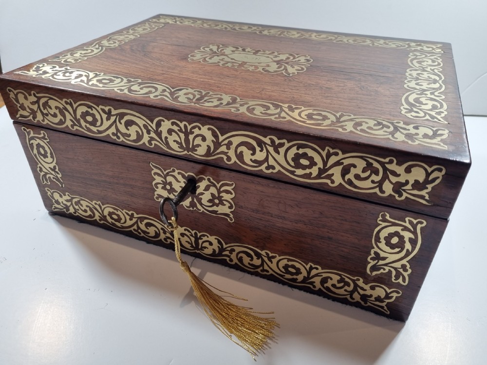 A rectangular dark rosewood writing box featuring intricate brass floral scrollwork inlay around the borders and escutcheon, complete with a key and tassel. View XII