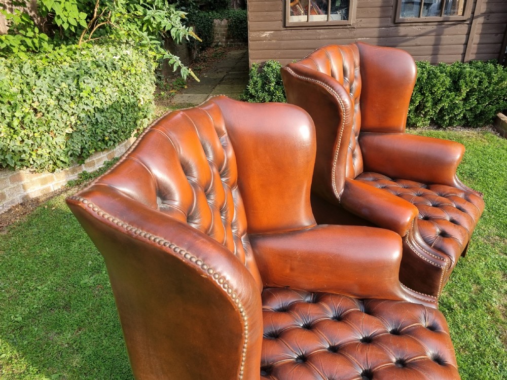 A pair of George III style chestnut brown leather Chesterfield wingback armchairs with deep buttoned upholstery, brass studding, and square wooden legs. View IX
