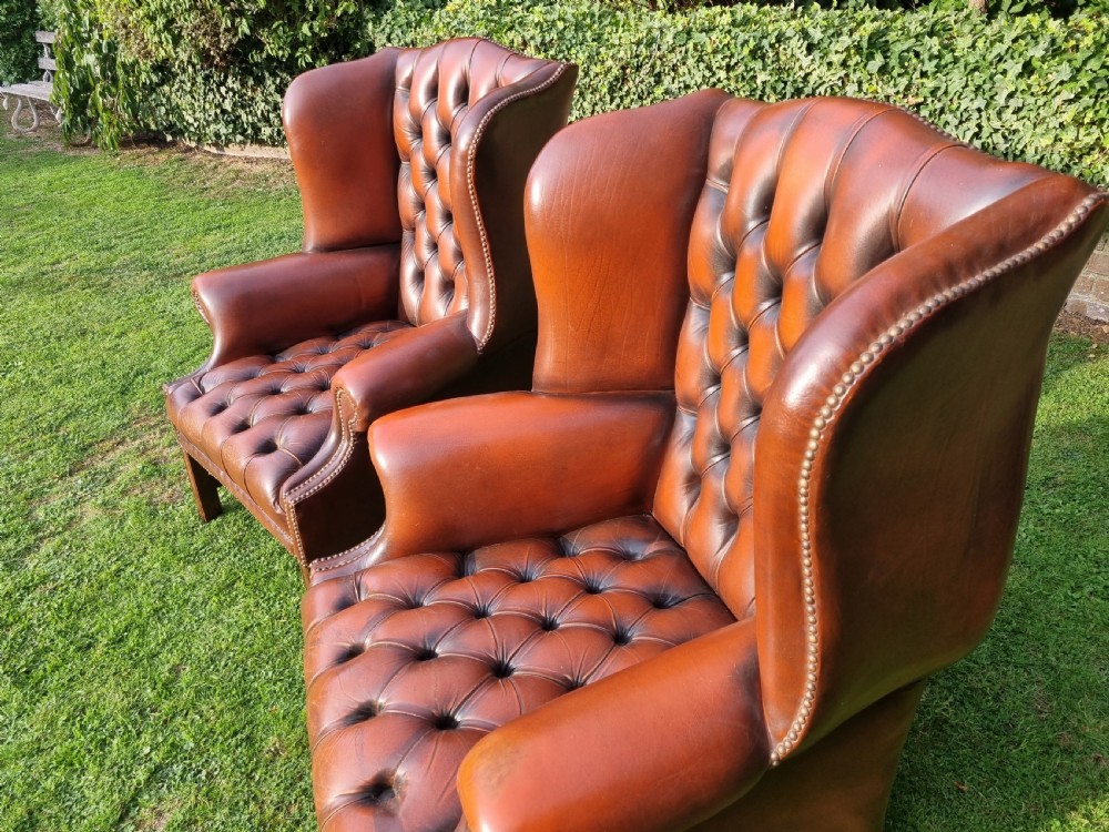 A pair of George III style chestnut brown leather Chesterfield wingback armchairs with deep buttoned upholstery, brass studding, and square wooden legs. View XI