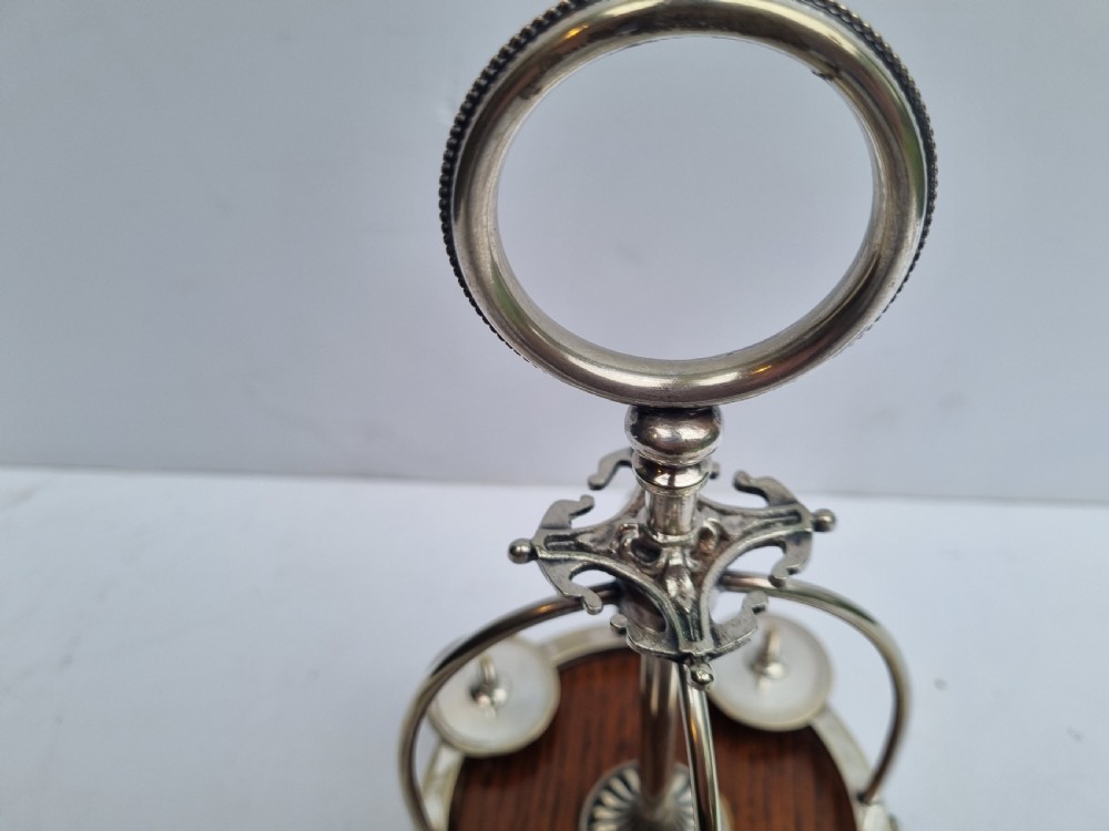 A Victorian silver-plated four-piece egg cruet featuring four goblets, four hanging spoons, a central carrying ring, and a circular oak base. View VII
