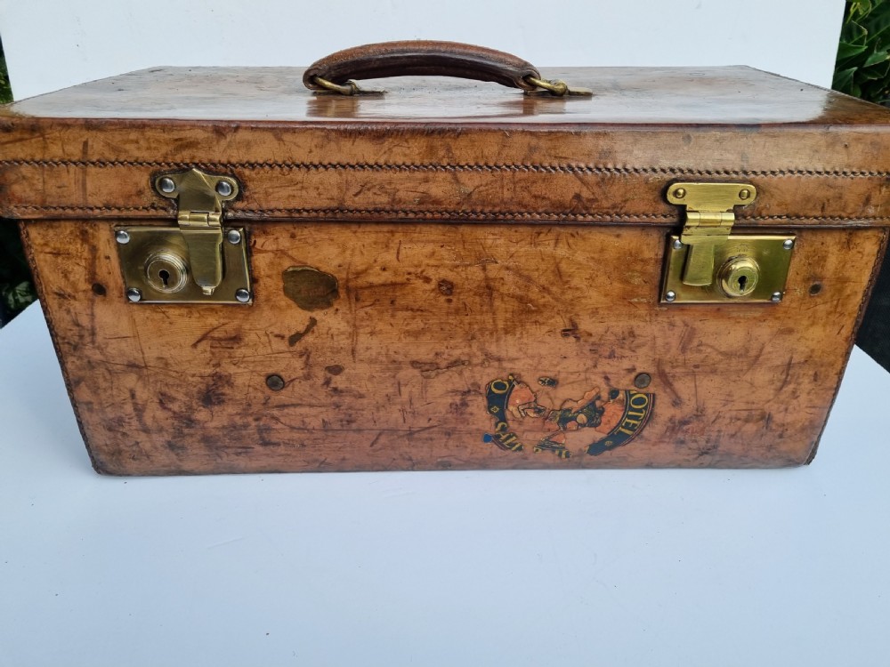A Victorian tan leather travel trunk featuring hand-stitched edges, brass lever locks, a top carrying handle, and patinated surface wear. View II