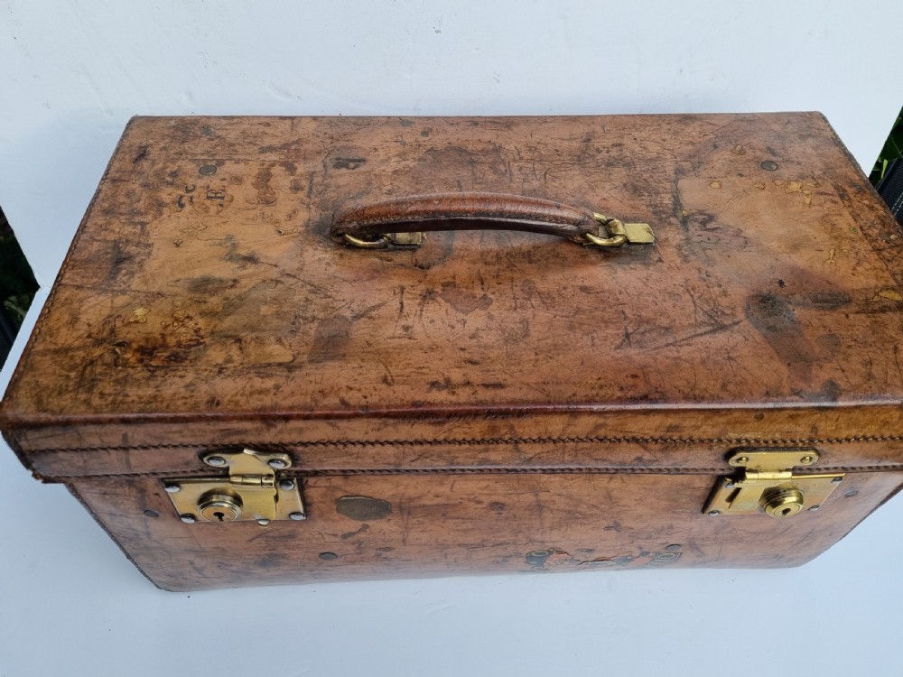 A Victorian tan leather travel trunk featuring hand-stitched edges, brass lever locks, a top carrying handle, and patinated surface wear. View III