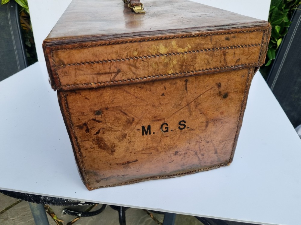 A Victorian tan leather travel trunk featuring hand-stitched edges, brass lever locks, a top carrying handle, and patinated surface wear. View V