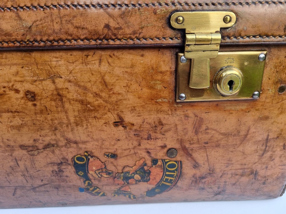 A Victorian tan leather travel trunk featuring hand-stitched edges, brass lever locks, a top carrying handle, and patinated surface wear. View IX