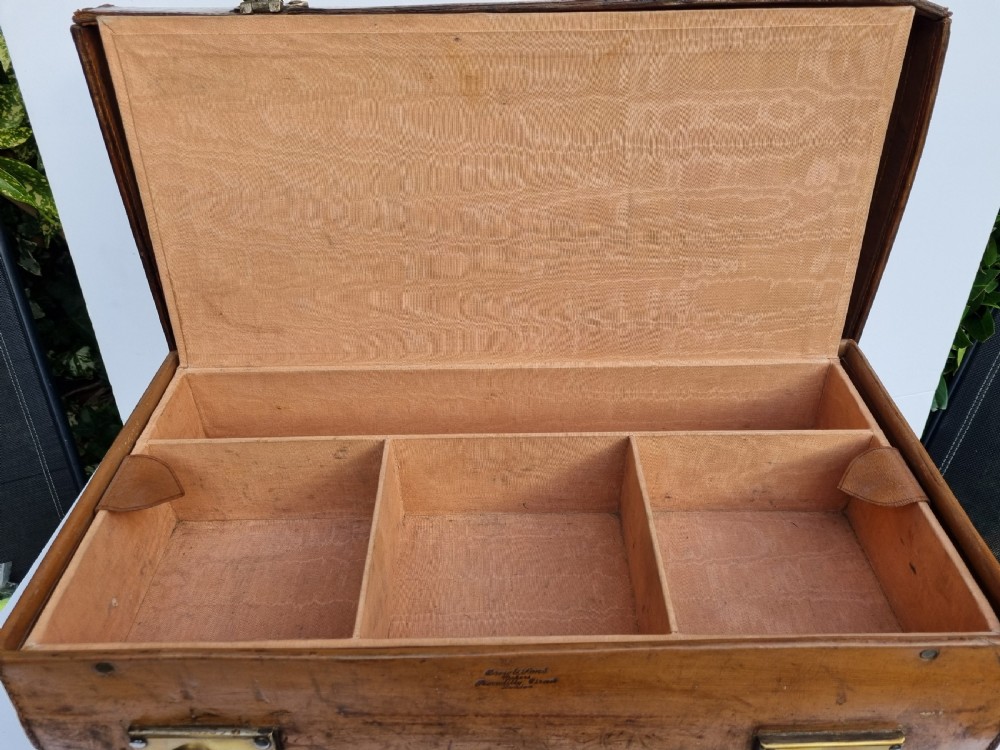 A Victorian tan leather travel trunk featuring hand-stitched edges, brass lever locks, a top carrying handle, and patinated surface wear. View XII