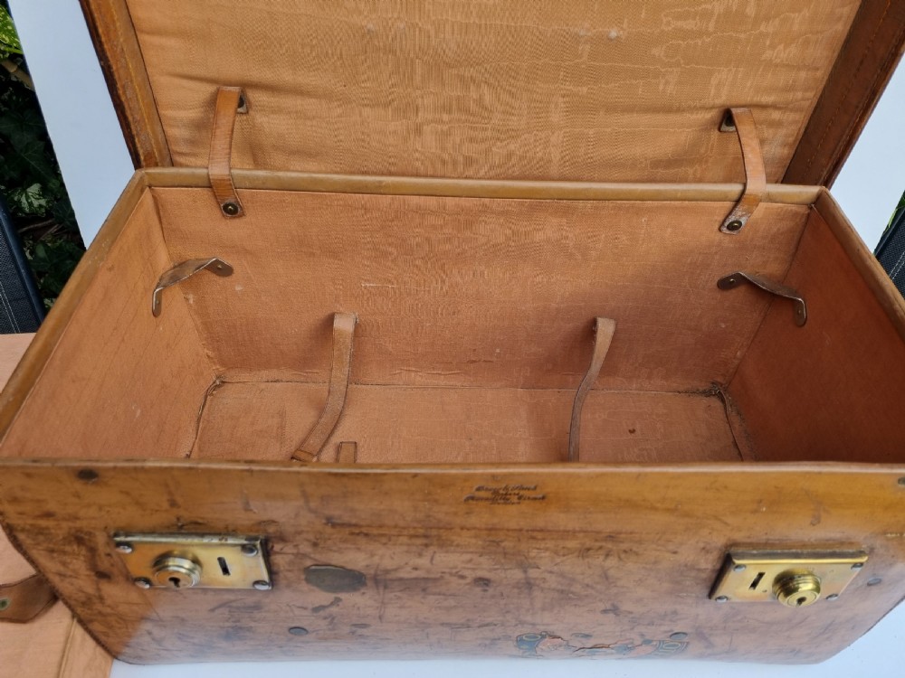 A Victorian tan leather travel trunk featuring hand-stitched edges, brass lever locks, a top carrying handle, and patinated surface wear. View XIII