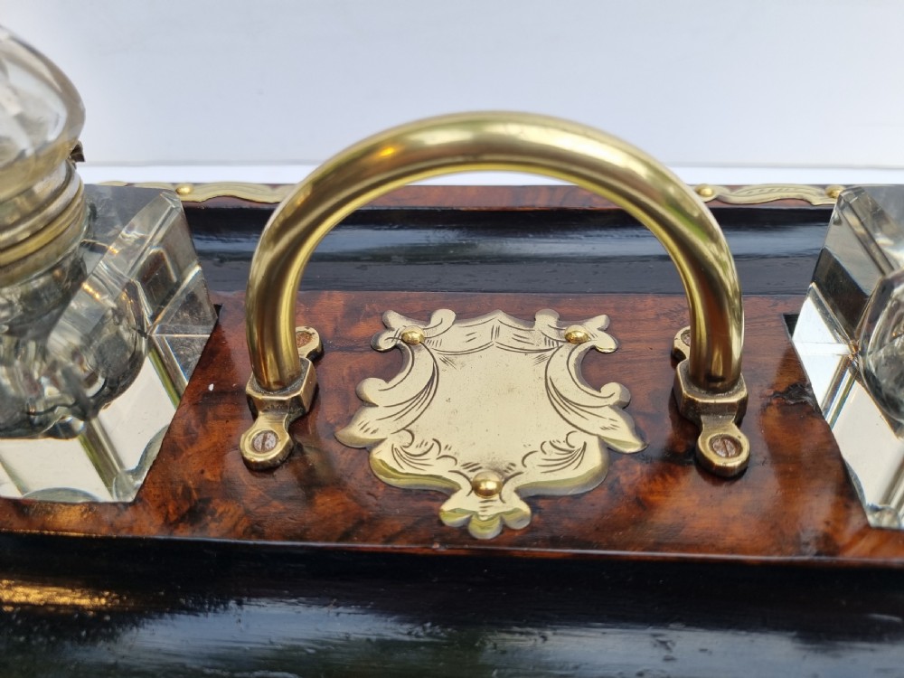 A Victorian walnut inkstand featuring two square glass inkwells, ornamental brass corner mounts, a central brass handle, a carved pen groove, and a lower drawer. View III