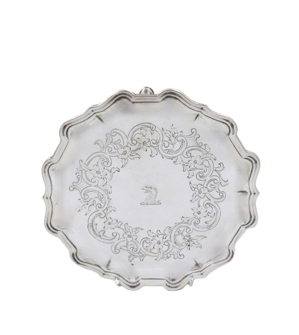 A circular 18th-century sterling silver card tray with a shaped piecrust rim, detailed scroll engraving, and a central heraldic crest.