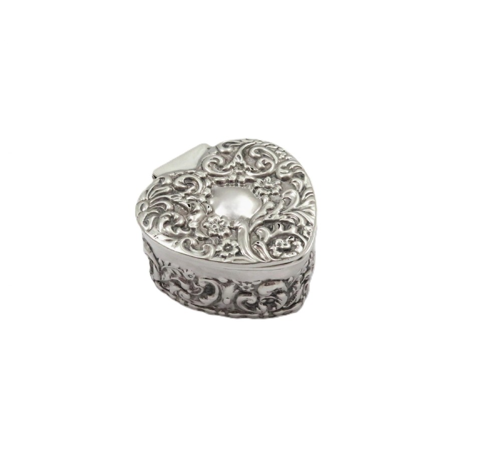 A small heart-shaped Edwardian sterling silver trinket box featuring detailed floral repousse scrolling across the lid and sides.