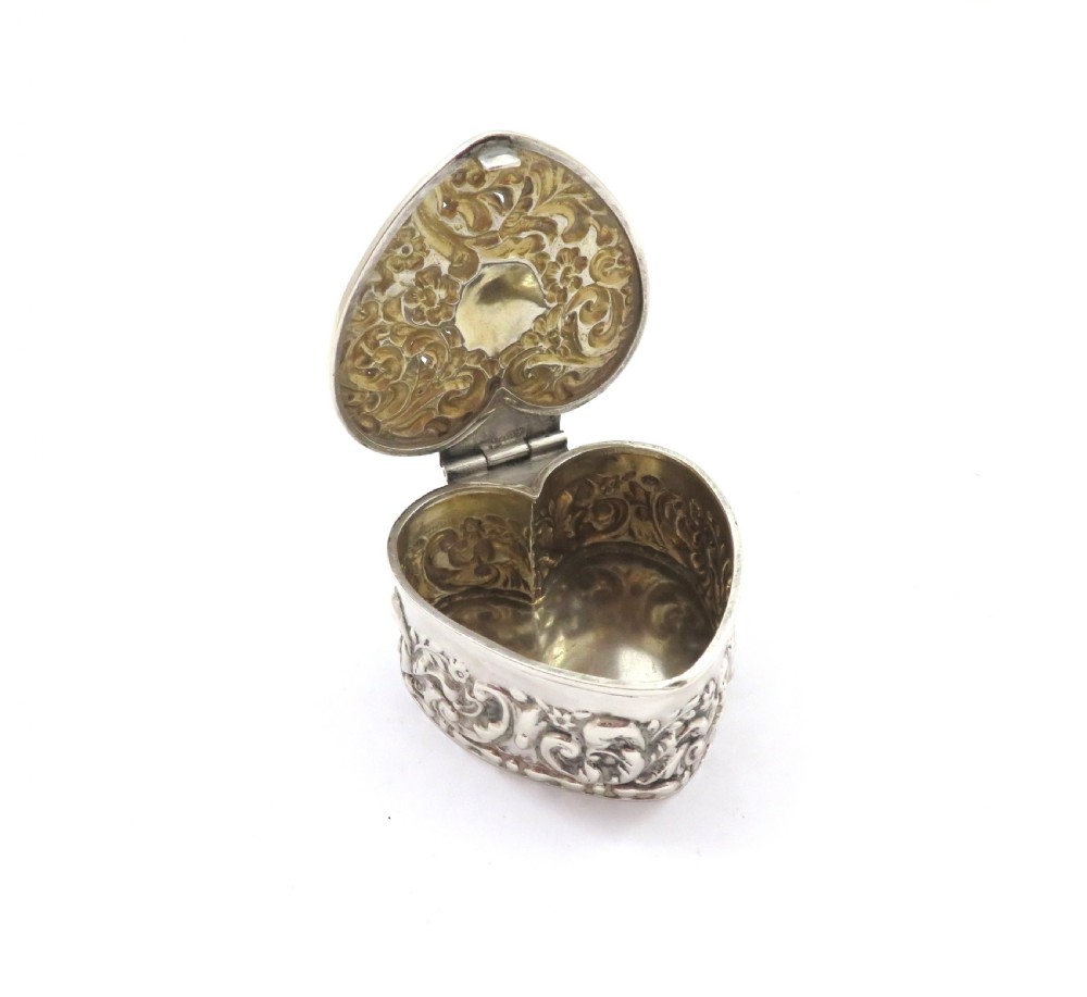 A small heart-shaped Edwardian sterling silver trinket box featuring detailed floral repousse scrolling across the lid and sides. View IV