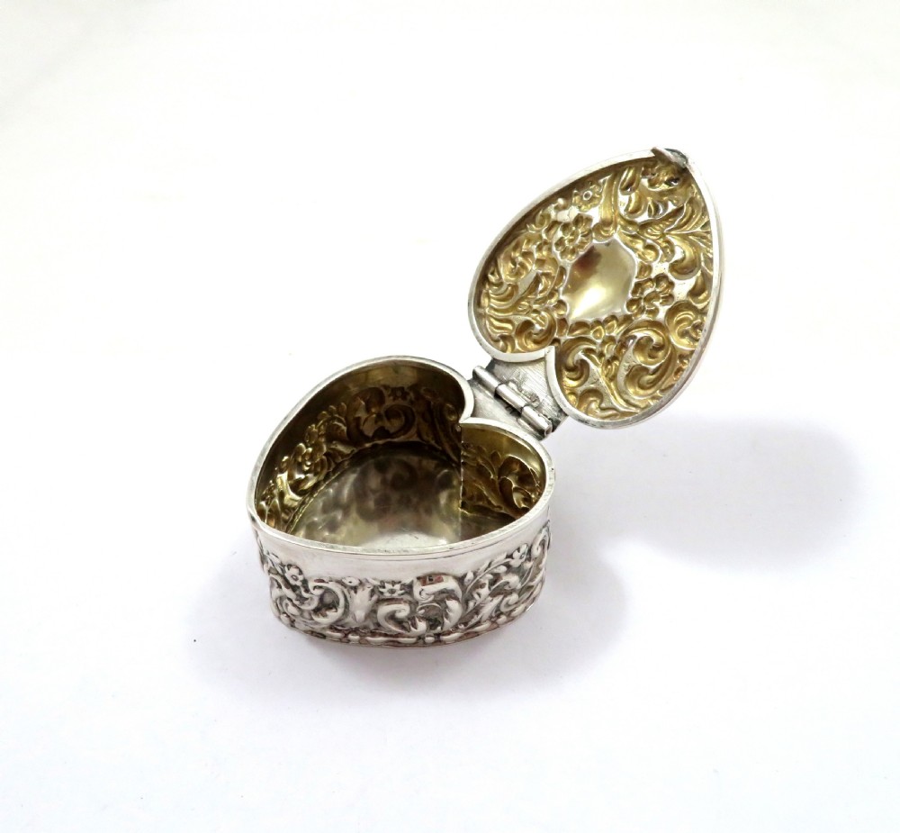 A small heart-shaped Edwardian sterling silver trinket box featuring detailed floral repousse scrolling across the lid and sides. View VI