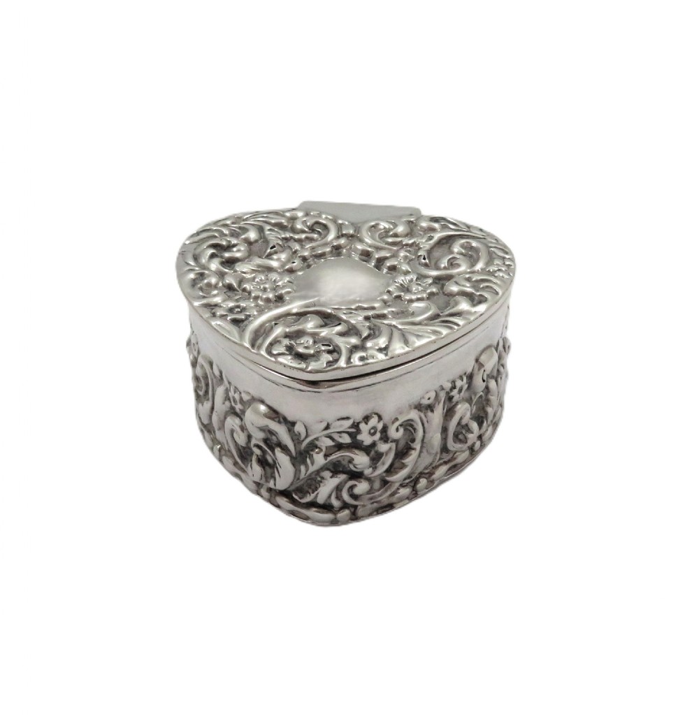A small heart-shaped Edwardian sterling silver trinket box featuring detailed floral repousse scrolling across the lid and sides. View IX