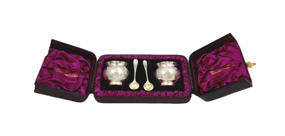 A pair of Victorian engraved sterling silver salt cellars with matching spoons displayed inside an open fitted purple silk-lined presentation case. View XII