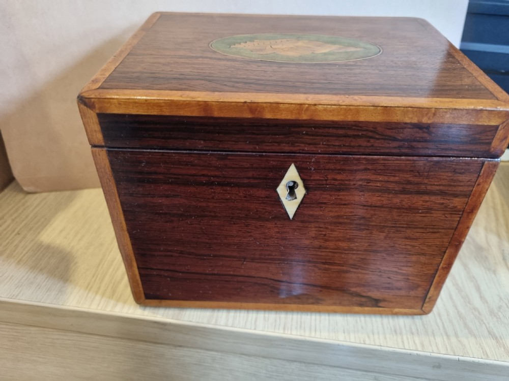 A rectangular dark rosewood tea caddy featuring a lid inlaid with an oval shell motif and a diamond-shaped bone keyhole escutcheon on the front face.