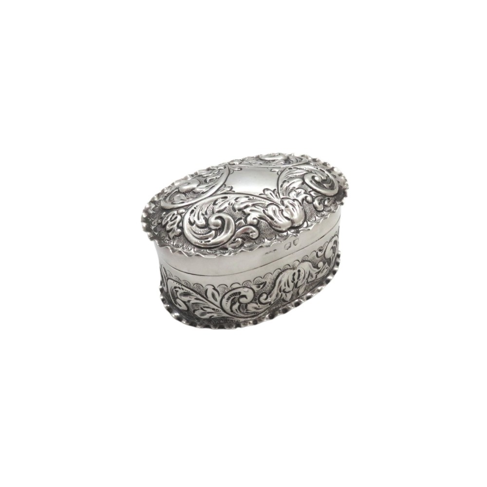 An oval antique sterling silver trinket box featuring detailed repousse scrollwork on the lid and sides.