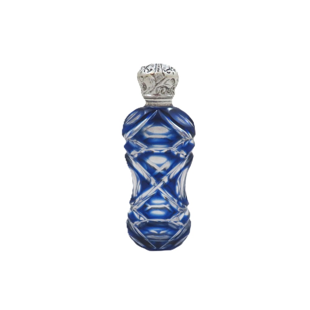 A Victorian cobalt blue overlay cut glass scent bottle featuring geometric cut patterns and an embossed silver cap.