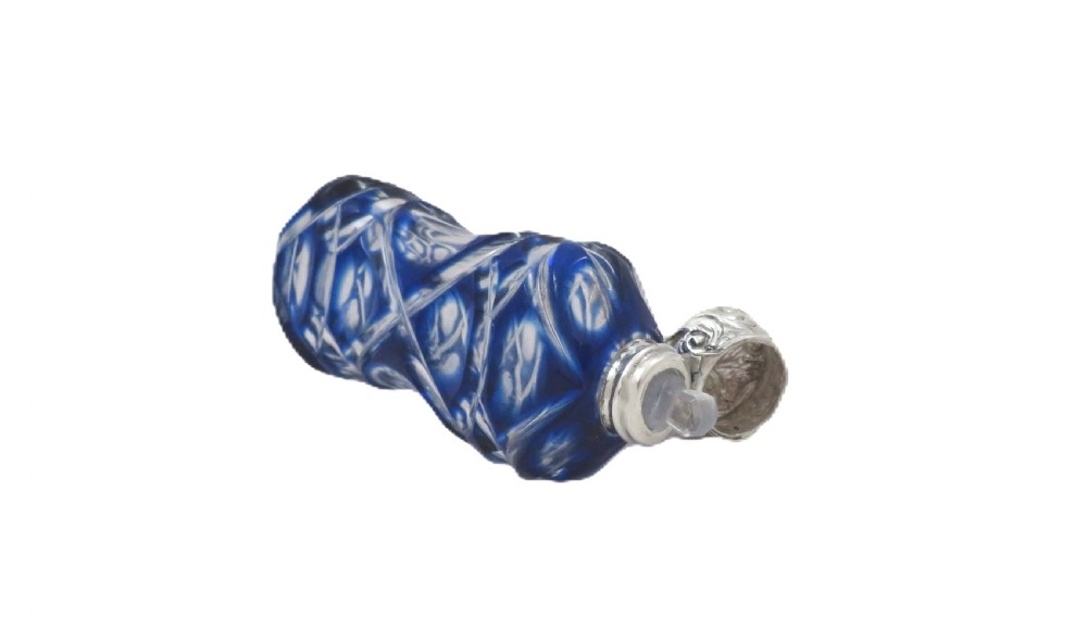 A Victorian cobalt blue overlay cut glass scent bottle featuring geometric cut patterns and an embossed silver cap. View VI