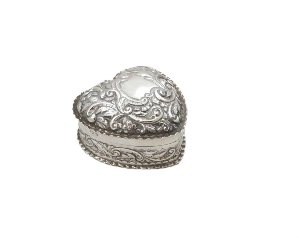 A heart-shaped sterling silver trinket box featuring detailed acanthus scroll repousse work around a smooth central cartouche. View IV