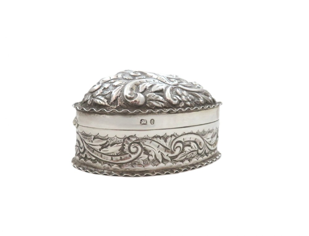 A heart-shaped sterling silver trinket box featuring detailed acanthus scroll repousse work around a smooth central cartouche. View V