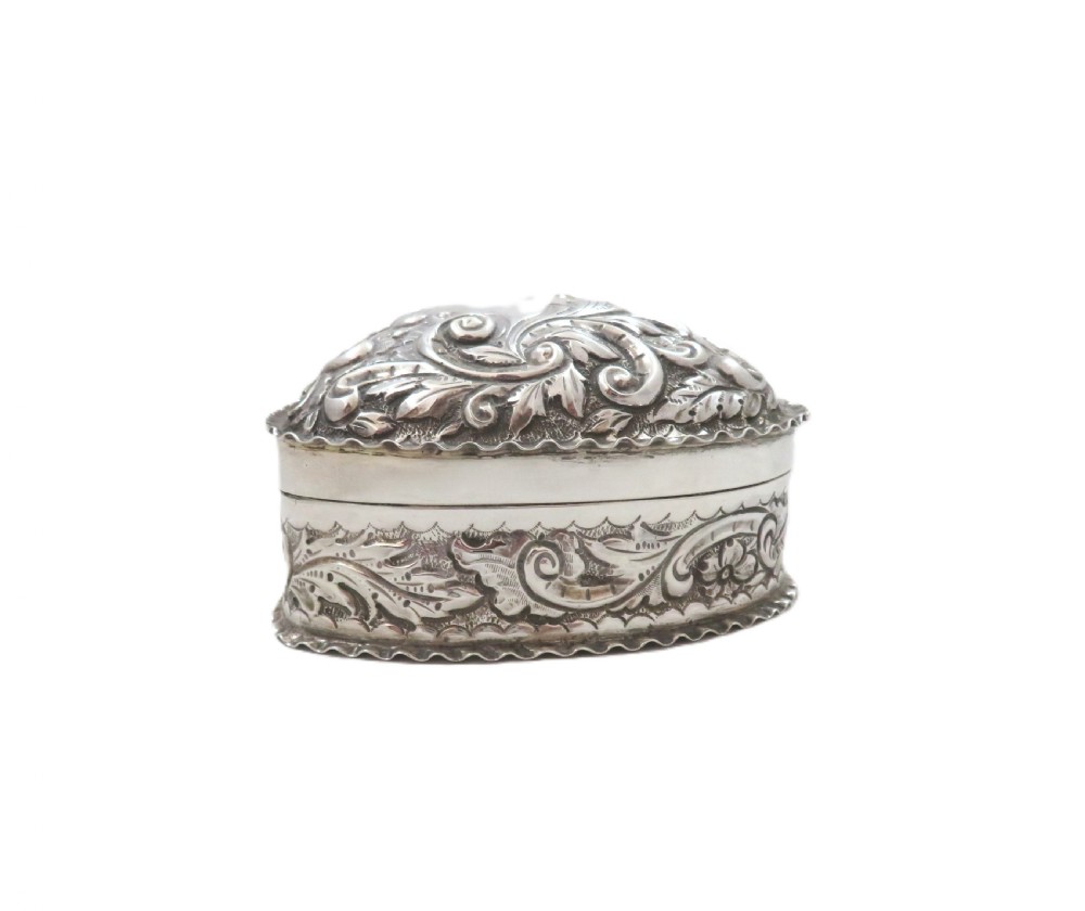 A heart-shaped sterling silver trinket box featuring detailed acanthus scroll repousse work around a smooth central cartouche. View VIII