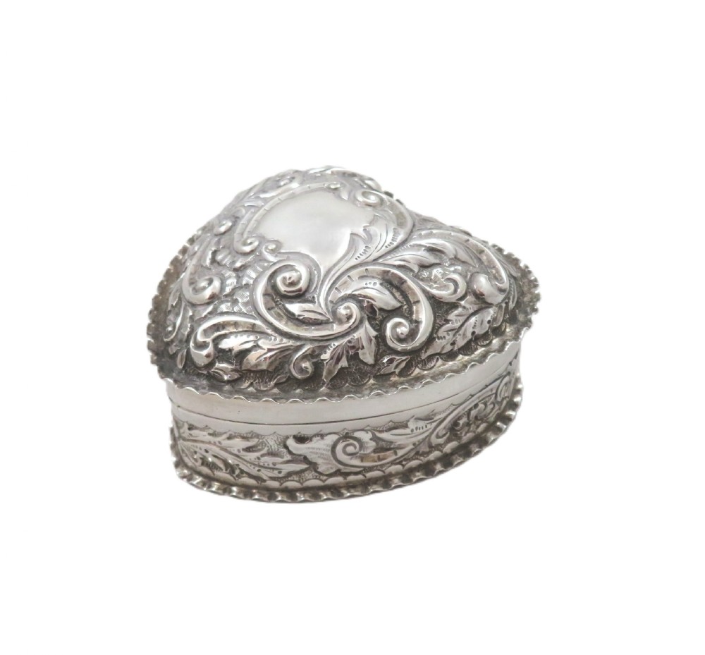 A heart-shaped sterling silver trinket box featuring detailed acanthus scroll repousse work around a smooth central cartouche. View IX
