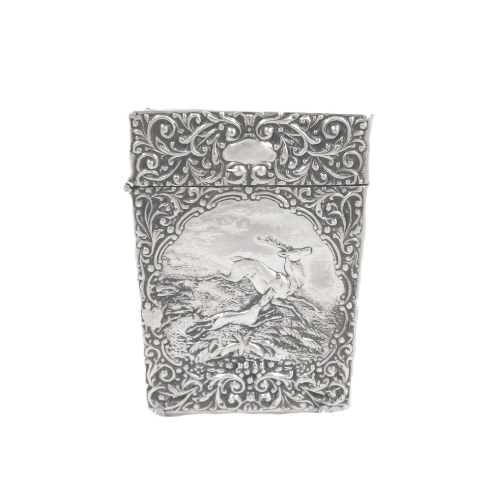 A rectangular Edwardian sterling silver card case decorated with repousse scrollwork and a central relief scene of a hound pursuing a stag.