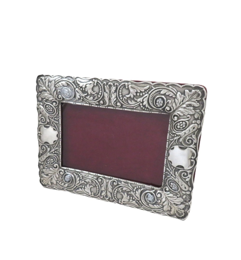 An Edwardian sterling silver landscape photo frame featuring repousse foliage motifs, a blank cartouche, and a dark velvet backing. View VIII