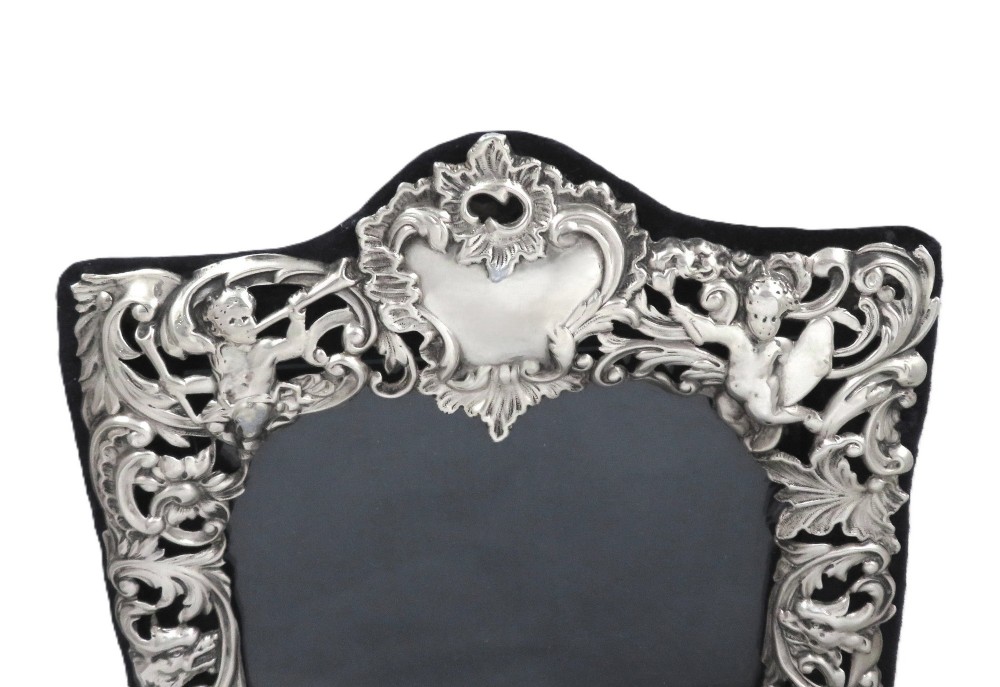 An antique Victorian sterling silver easel photo frame featuring a heart-shaped central opening surrounded by embossed cherubs, foliate scrolls, and a blank top cartouche. View IV