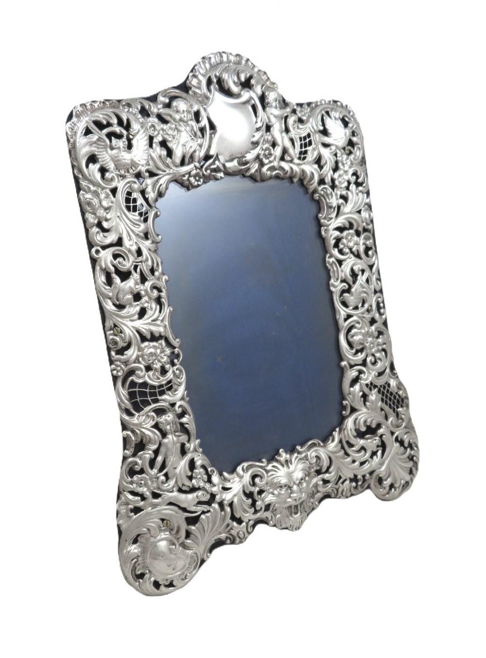 An ornate late Victorian sterling silver photo frame featuring intricate pierced scrollwork, cherub figures, birds, and a central lion mask at the base. View IV