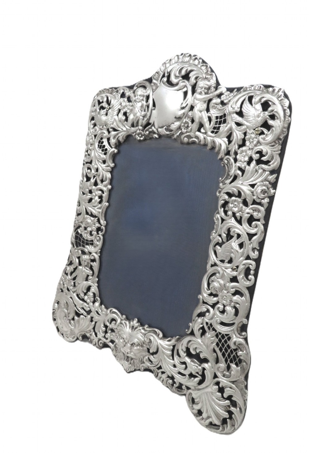 An ornate late Victorian sterling silver photo frame featuring intricate pierced scrollwork, cherub figures, birds, and a central lion mask at the base. View VIII
