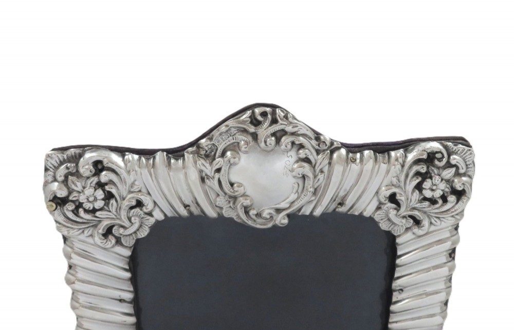 An antique Edwardian sterling silver picture frame featuring fluted borders, floral repousse details, a central top cartouche, and an easel backing. View III