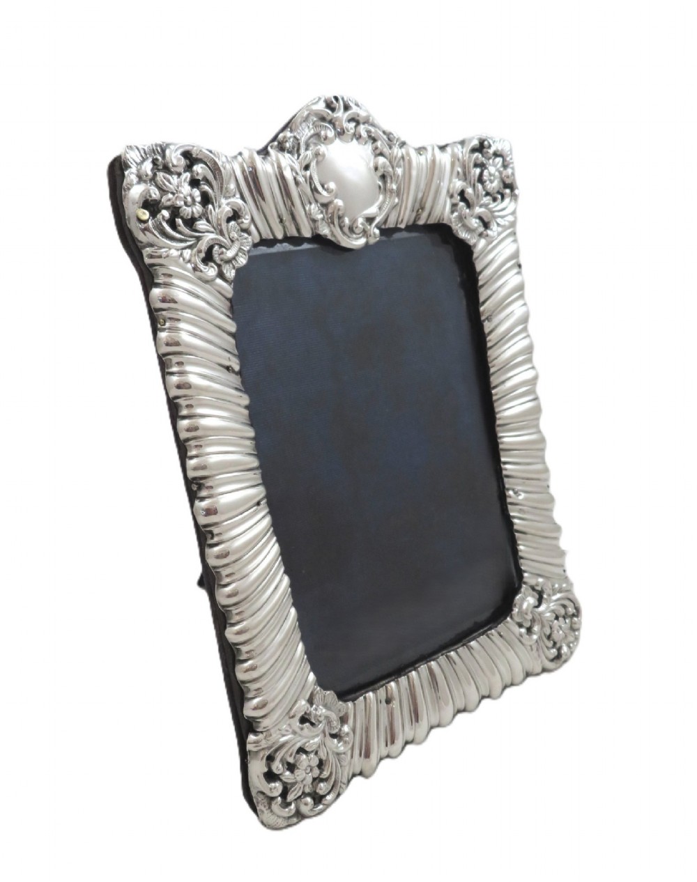 An antique Edwardian sterling silver picture frame featuring fluted borders, floral repousse details, a central top cartouche, and an easel backing. View VII