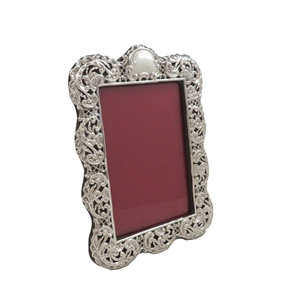 An antique Victorian sterling silver photo frame featuring intricate scrollwork, pierced openwork detail, a rectangular aperture, and a maroon backing.