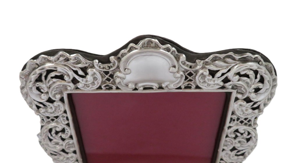 An antique Victorian sterling silver photo frame featuring intricate scrollwork, pierced openwork detail, a rectangular aperture, and a maroon backing. View III