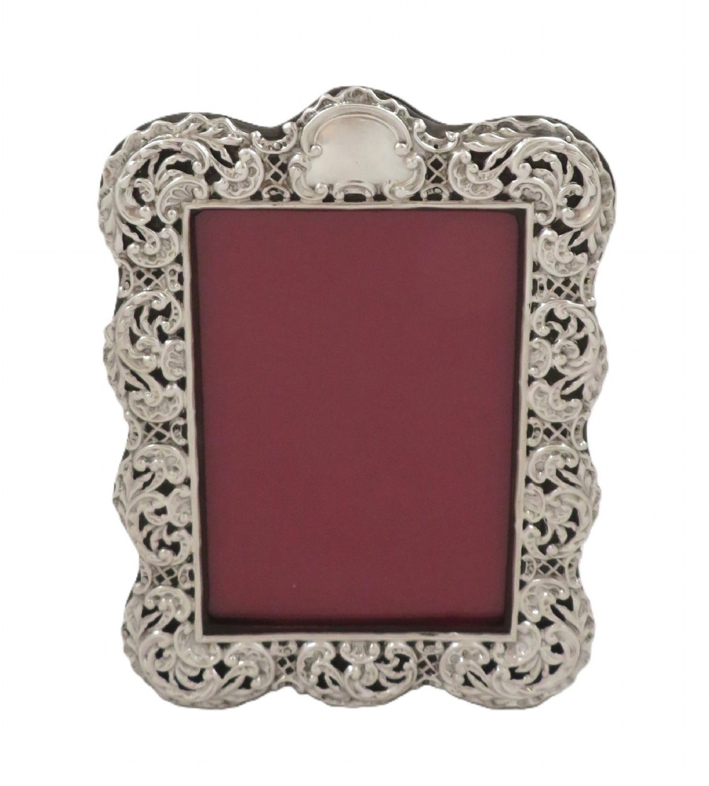An antique Victorian sterling silver photo frame featuring intricate scrollwork, pierced openwork detail, a rectangular aperture, and a maroon backing. View V