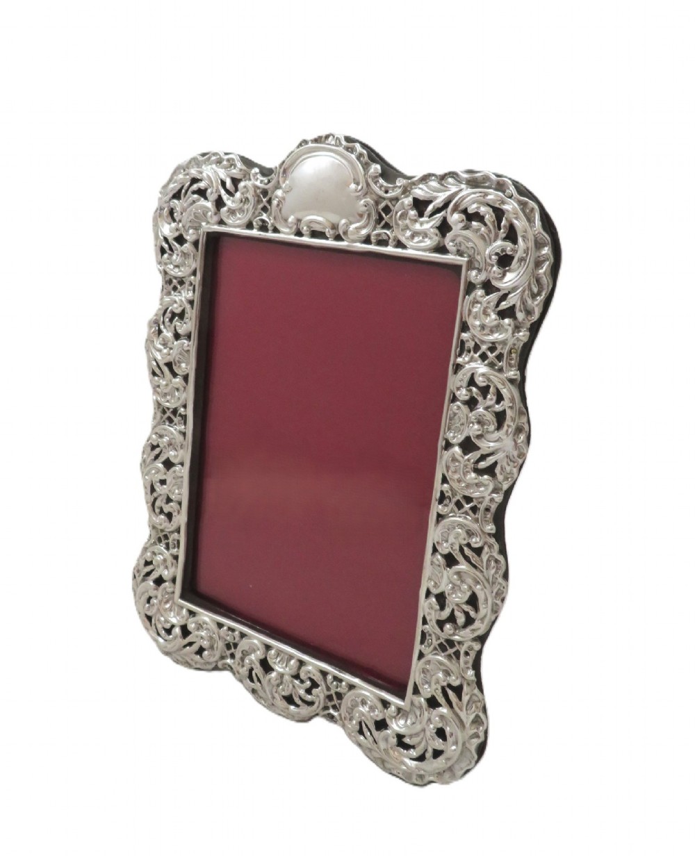 An antique Victorian sterling silver photo frame featuring intricate scrollwork, pierced openwork detail, a rectangular aperture, and a maroon backing. View VI