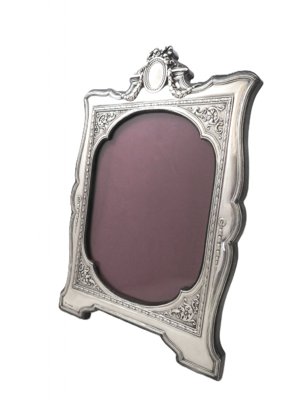 An ornate Edwardian sterling silver portrait photo frame featuring a ribbon crest and shaped border, resting on an easel back. View VII