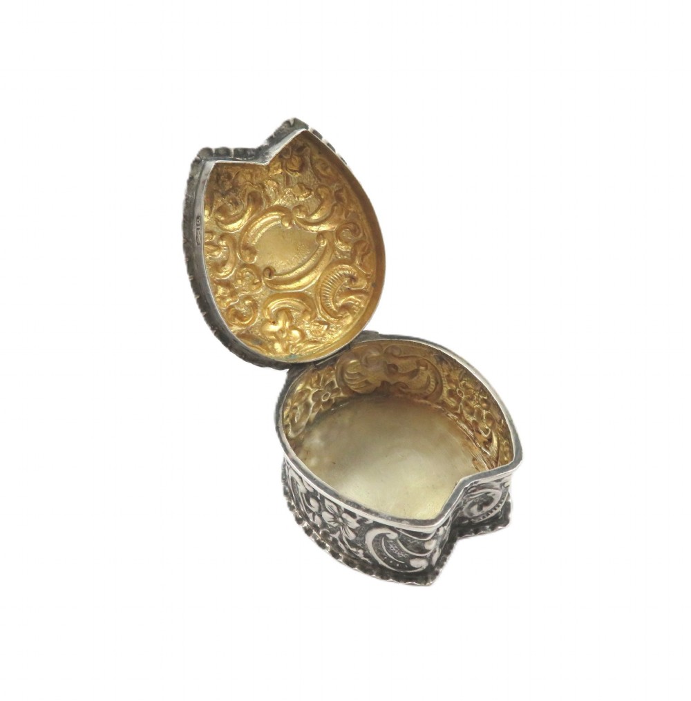 A small horseshoe-shaped sterling silver trinket box featuring embossed floral scrollwork and a central vacant cartouche. View III