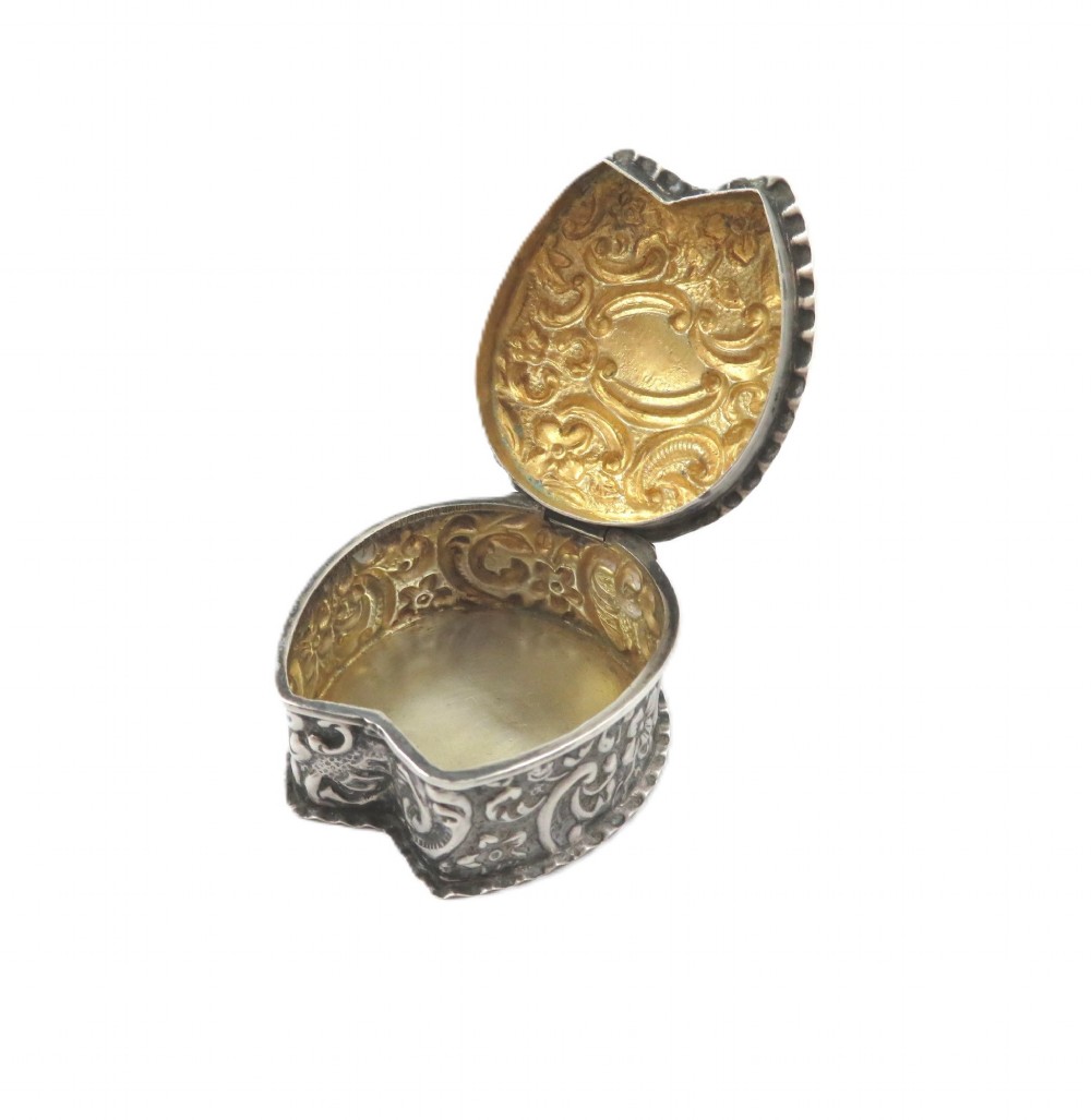 A small horseshoe-shaped sterling silver trinket box featuring embossed floral scrollwork and a central vacant cartouche. View VII