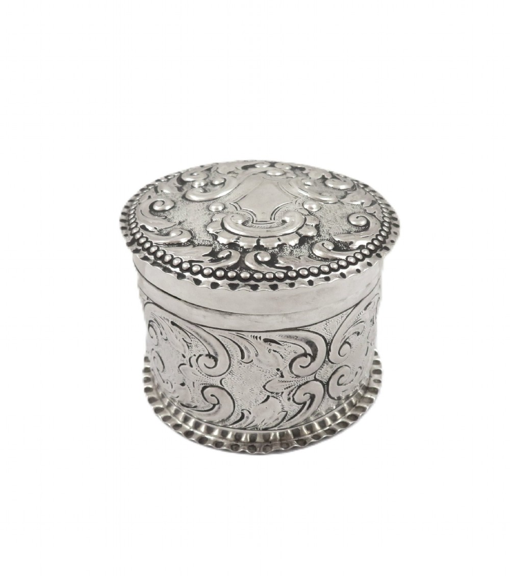 A small cylindrical Victorian sterling silver vanity pot decorated with floral repousse scrollwork and a beaded rim around the lid.