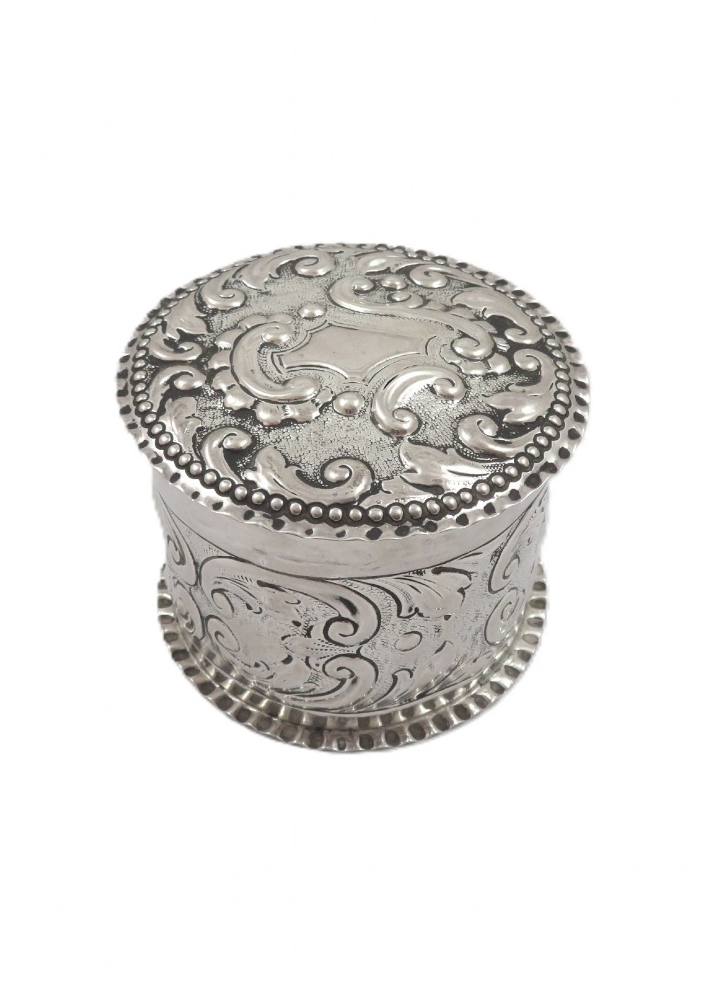 A small cylindrical Victorian sterling silver vanity pot decorated with floral repousse scrollwork and a beaded rim around the lid. View IV