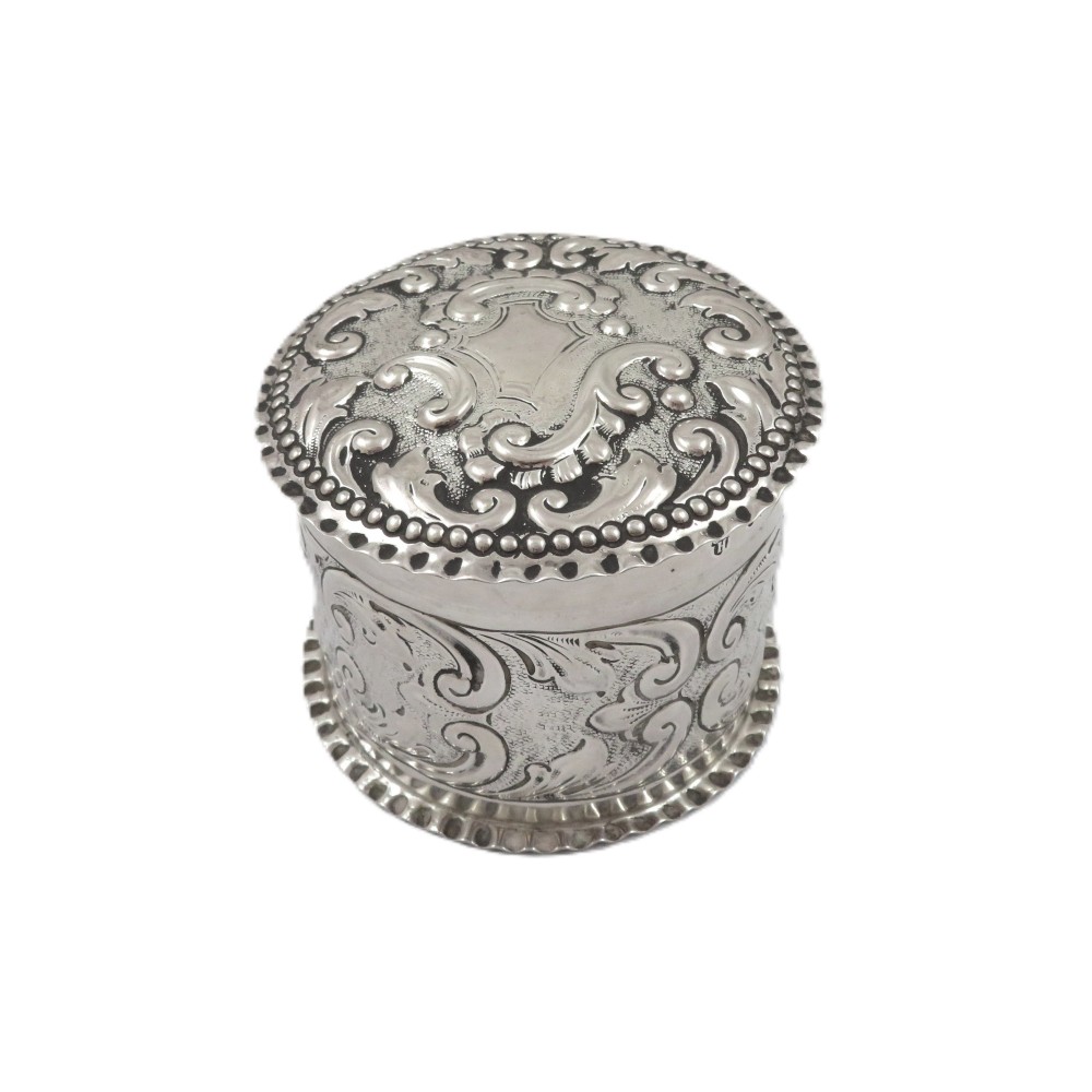 A small cylindrical Victorian sterling silver vanity pot decorated with floral repousse scrollwork and a beaded rim around the lid. View VI