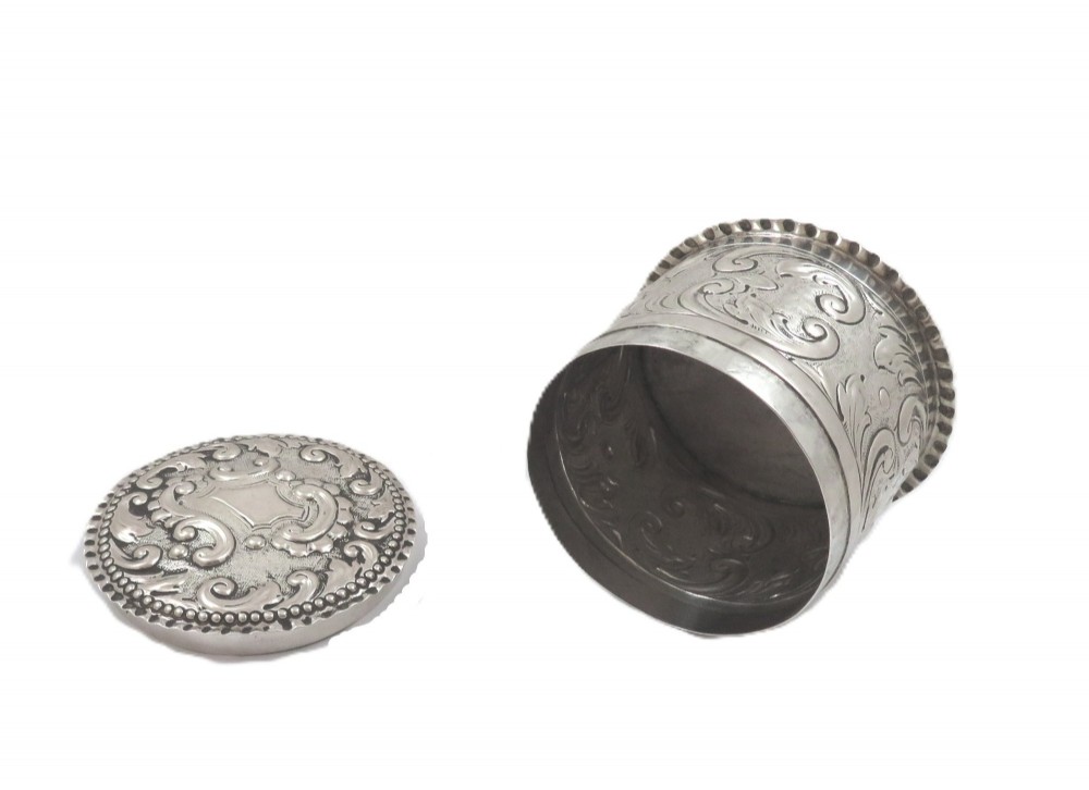 A small cylindrical Victorian sterling silver vanity pot decorated with floral repousse scrollwork and a beaded rim around the lid. View VII