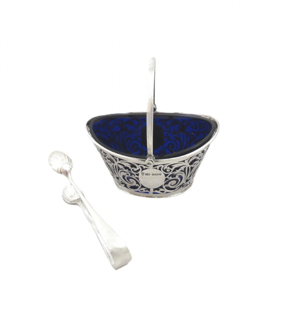 An Edwardian hallmarked sterling silver pierced sugar basket with a cobalt blue glass liner and matching silver sugar tongs in an open presentation case. View VI
