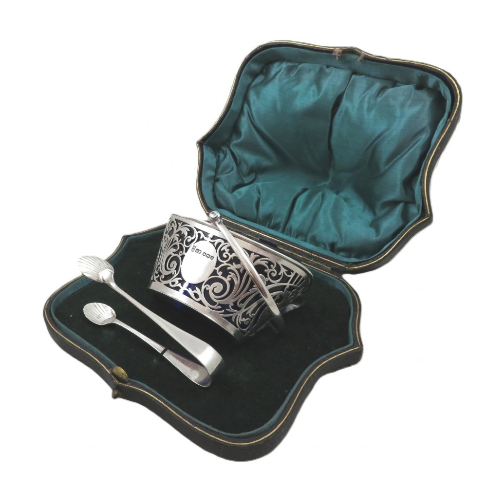 An Edwardian hallmarked sterling silver pierced sugar basket with a cobalt blue glass liner and matching silver sugar tongs in an open presentation case. View VII