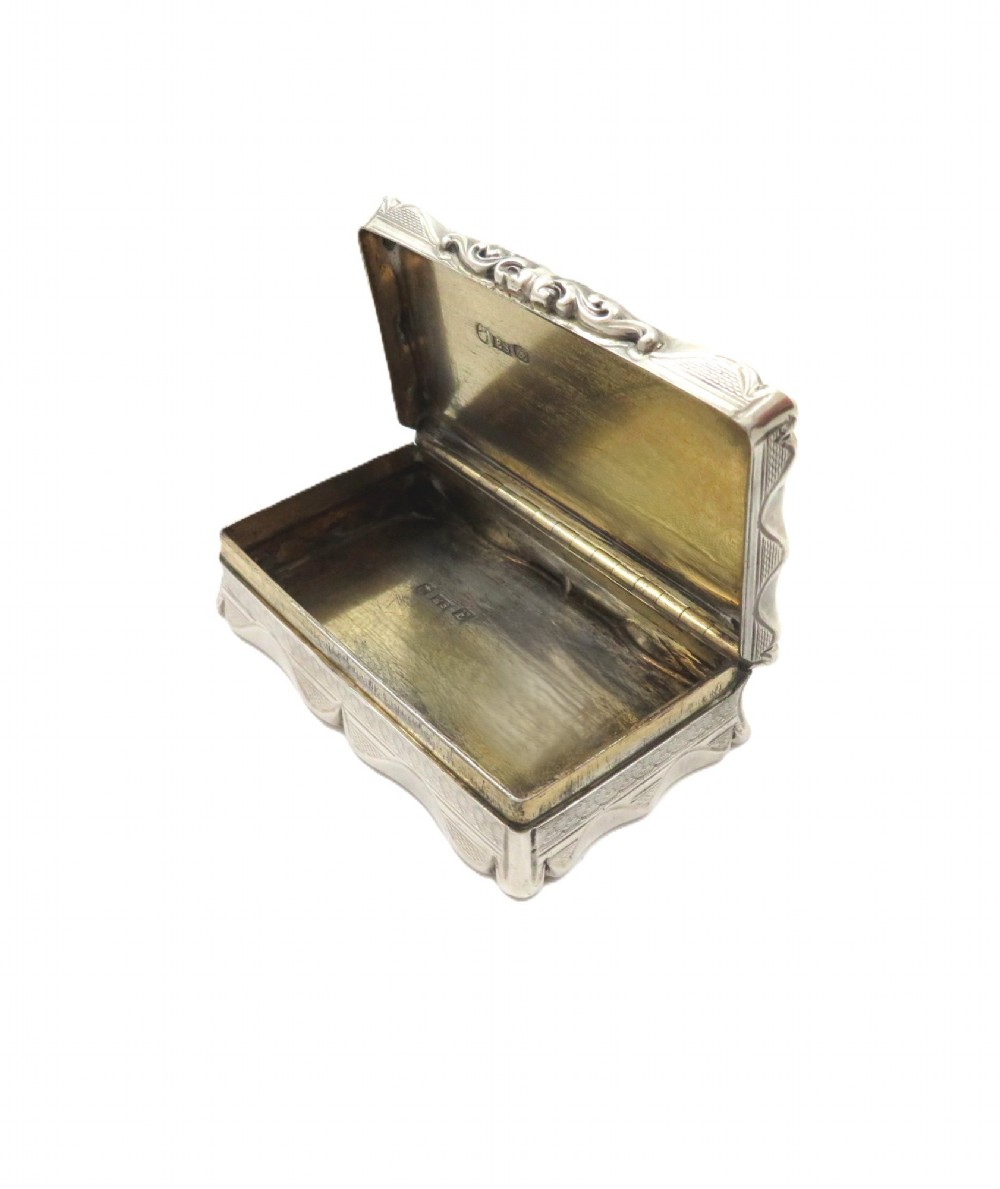 A rectangular Victorian sterling silver snuff box featuring scalloped edges, engine-turned linear engraving, and an unengraved scrollwork cartouche on the lid. View III