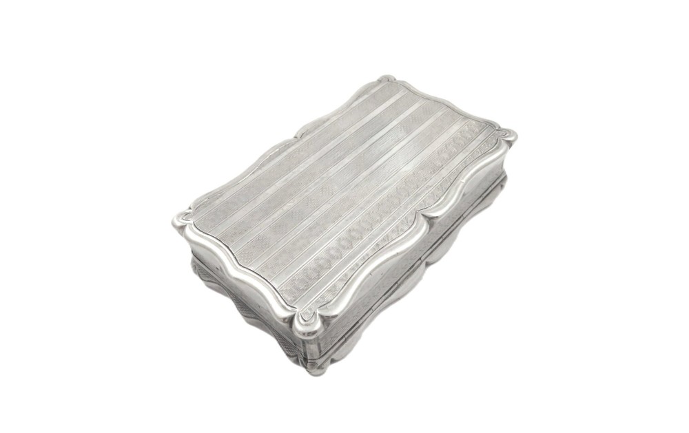 A rectangular Victorian sterling silver snuff box featuring scalloped edges, engine-turned linear engraving, and an unengraved scrollwork cartouche on the lid. View IV