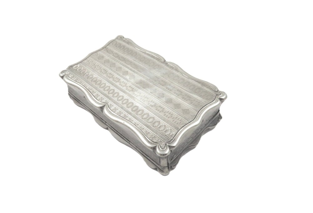 A rectangular Victorian sterling silver snuff box featuring scalloped edges, engine-turned linear engraving, and an unengraved scrollwork cartouche on the lid. View IX
